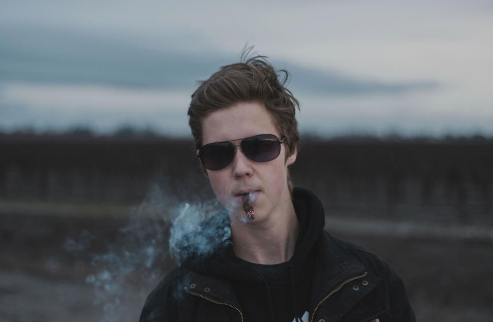 Free Image of A man wearing sunglasses and smoking a cigar 
