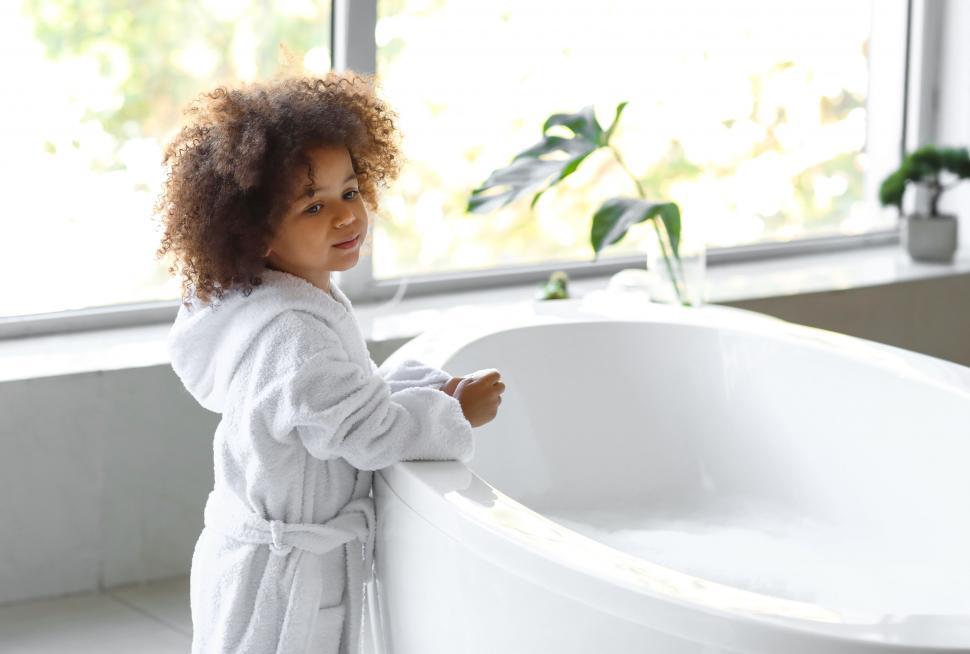 Free Image of Curly-haired child peering into bathtub 