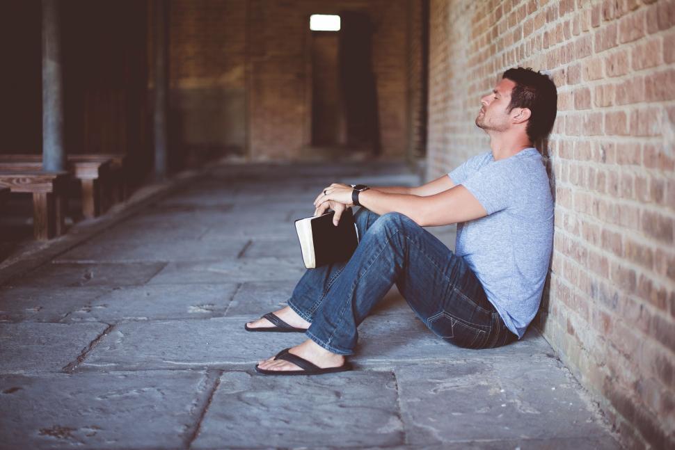 Free Image of Man sitting and reading against brick wall 