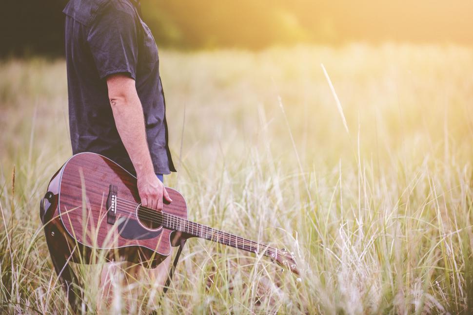 Free Image of Man holding guitar in grassy field at sunset 