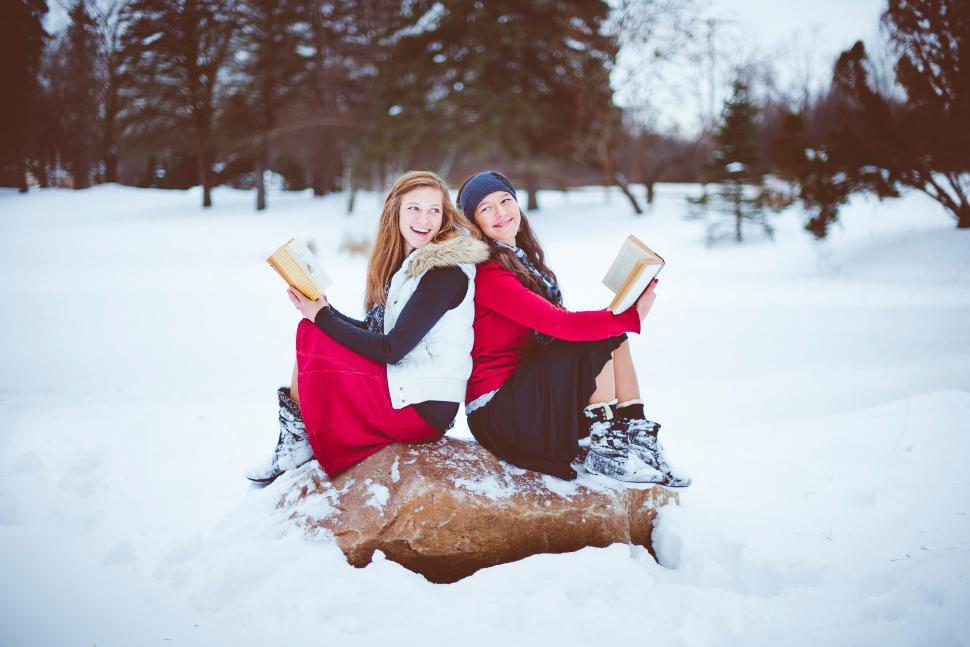 Free Image of Two friends reading books in winter snow 