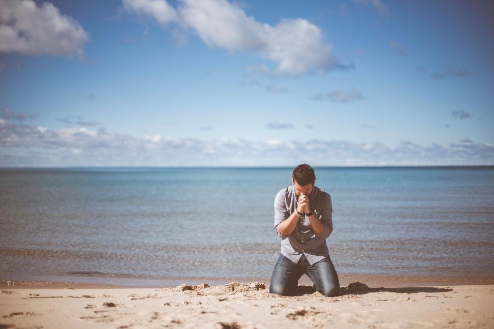 Free Image of Solitary man praying on sandy beach 