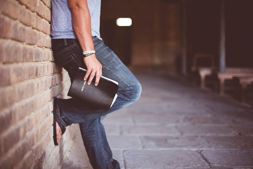 Free Image of Man leaning on a brick wall with a Bible 