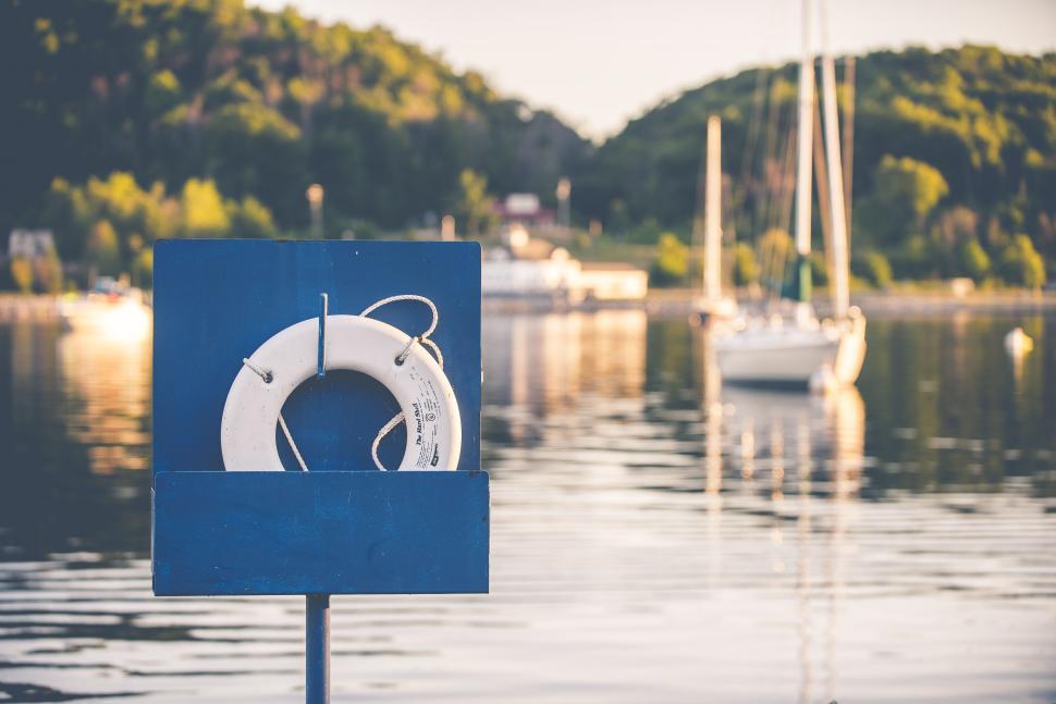 Free Image of Lifebuoy on post with lake and boats behind 
