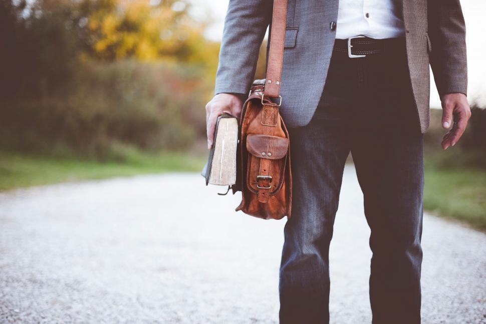 Free Image of Man walking on path with book and leather bag 
