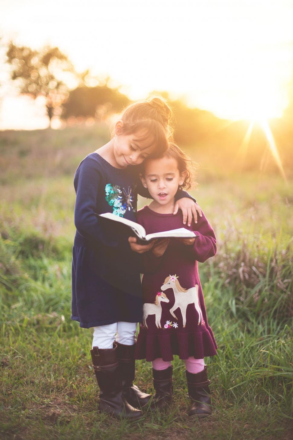 Free Image of Sisters reading a book together in field 