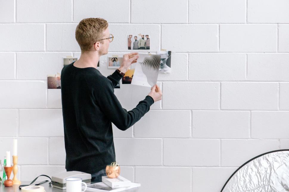 Free Image of Man arranging photos on a white wall 
