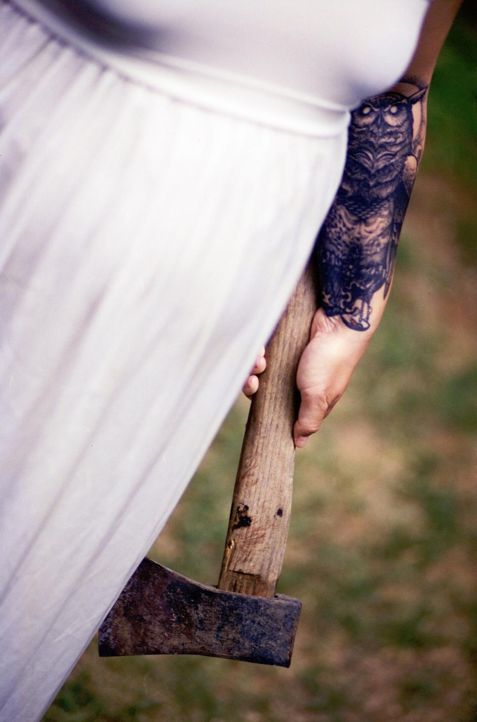 Free Image of Tattooed hand holding an axe by a white dress 
