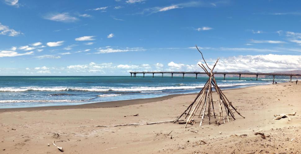 Free Image of Driftwood structure on sandy beach with pier 