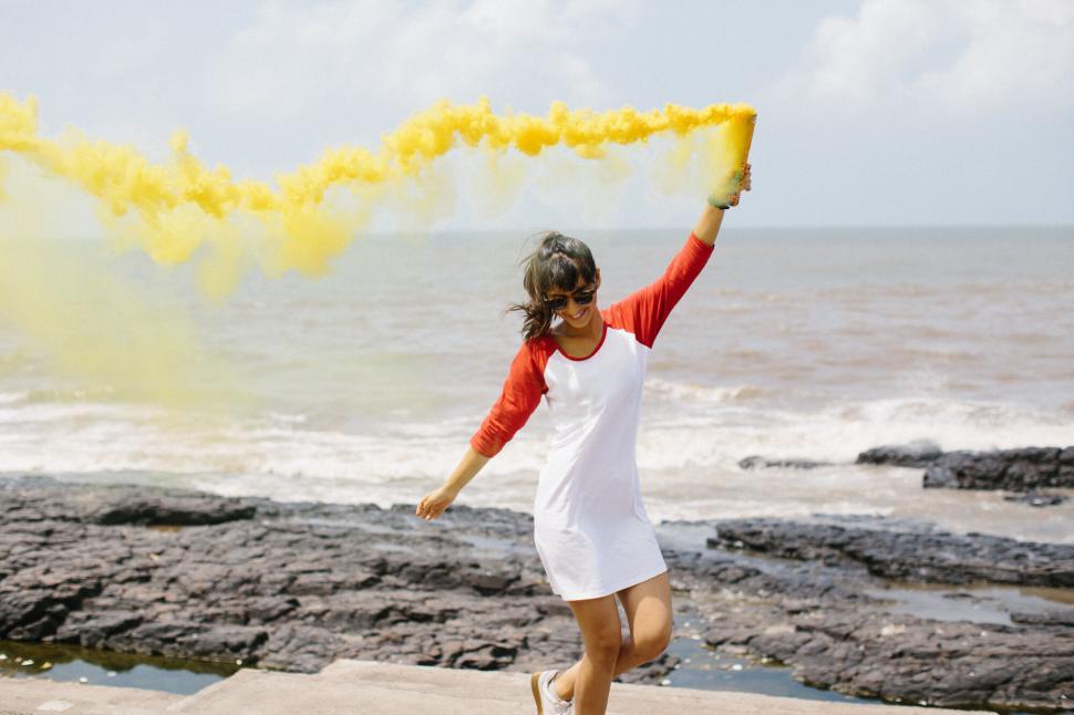 Free Image of Woman holding yellow smoke on beach 