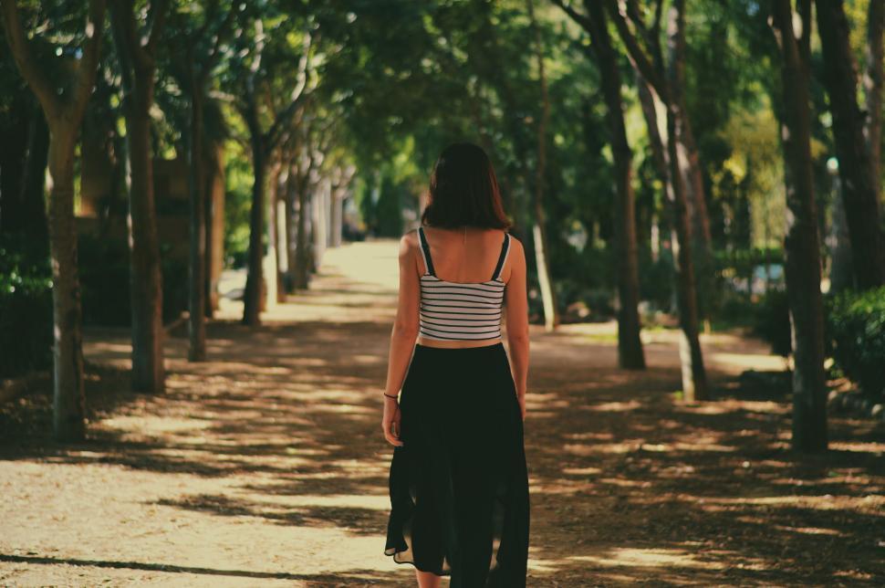 Free Image of Woman walking down a tree-lined path 