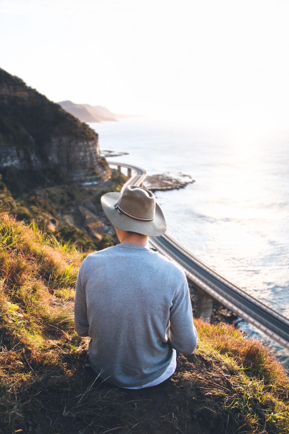 Free Image of Man looking at coastal road from hilltop 