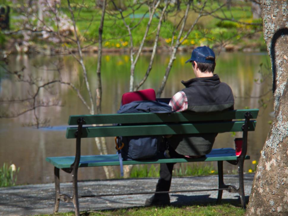 Free Image of Person relaxing on a park bench by a lake 