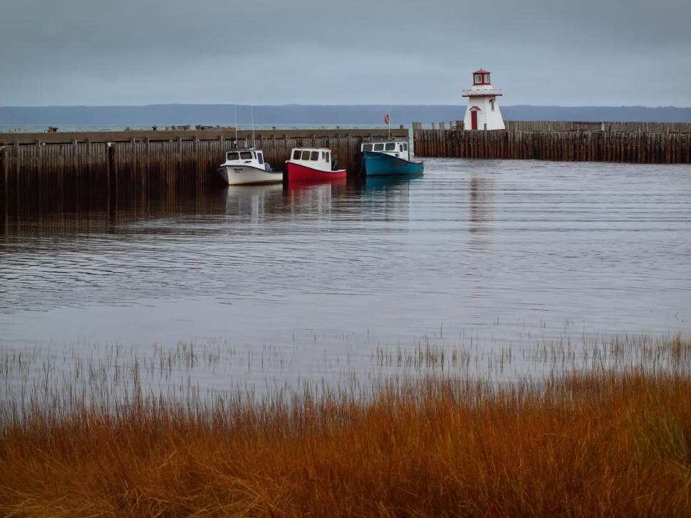 Free Image of Serene harbor scene with boats and a lighthouse 