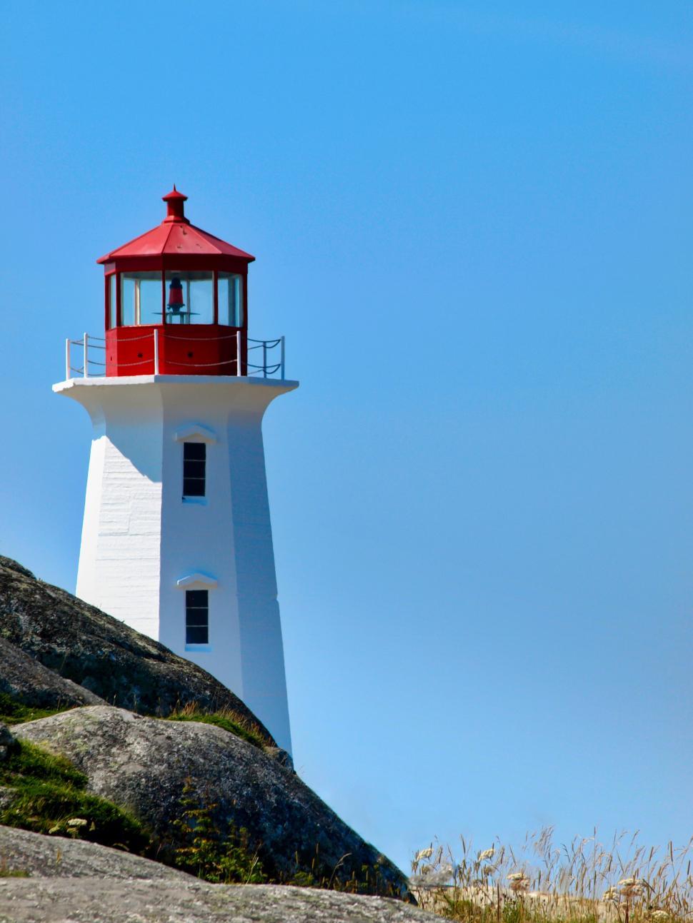 Free Image of Lighthouse on rocky coastline under blue sky 