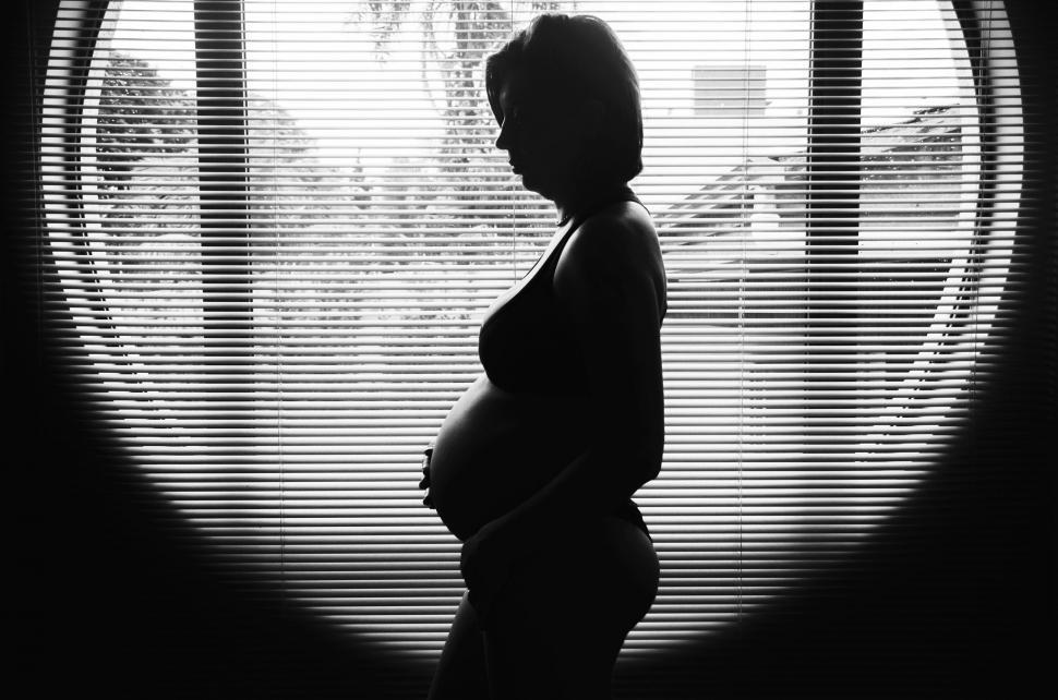 Free Image of Silhouetted pregnant woman against window blinds 