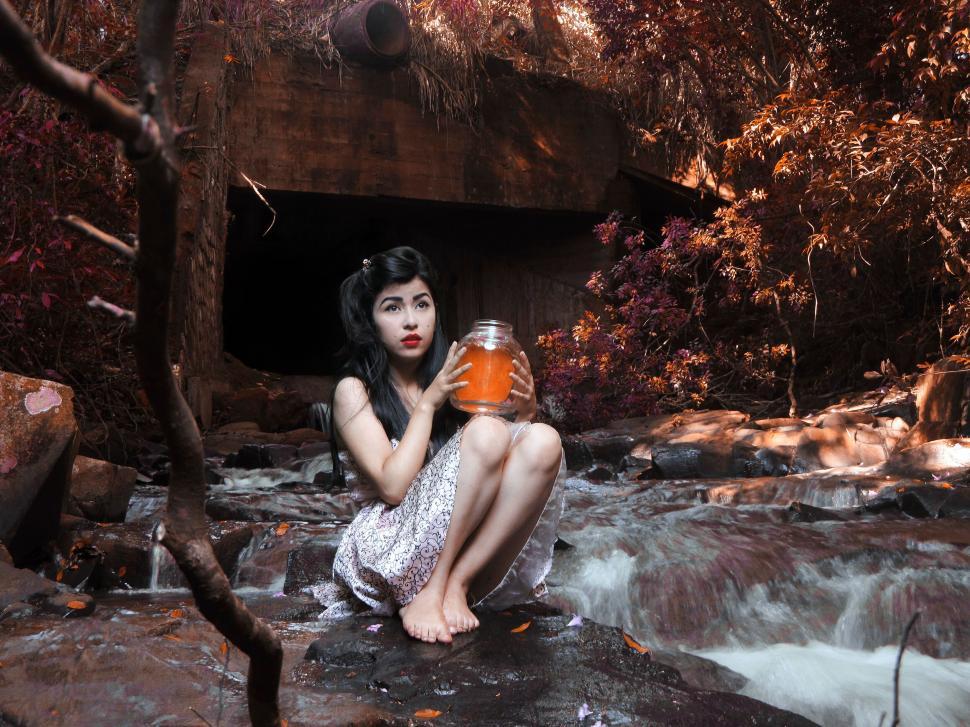 Free Image of Girl with jar sitting by stream 