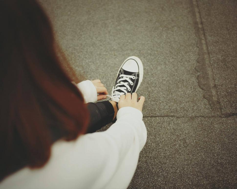 Free Image of Woman tying shoelaces on city sidewalk 