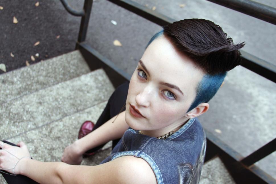 Free Image of Young person with blue hair sitting on steps 