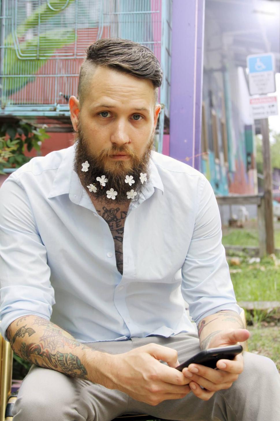 Free Image of Man with beard and flowers texting on phone 