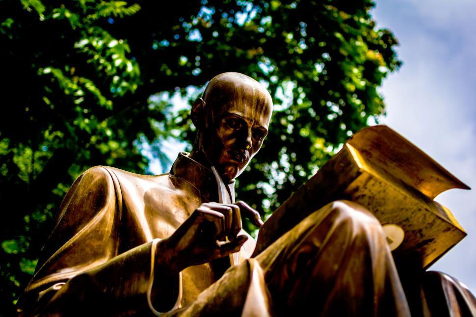 Free Image of Bronze statue reading a book against trees 