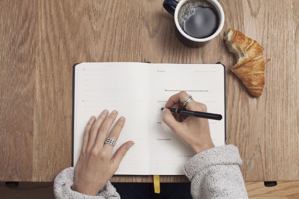 Free Image of Hands writing in planner with coffee and pastry 