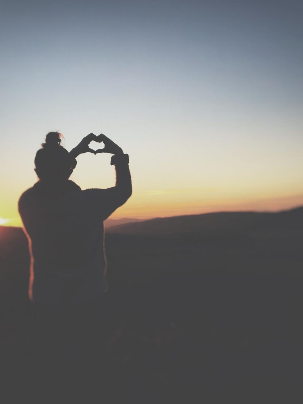 Free Image of Silhouette making heart shape with hands at sunset 