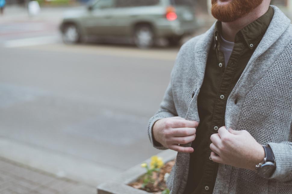 Free Image of Man buttoning up cardigan on city street 
