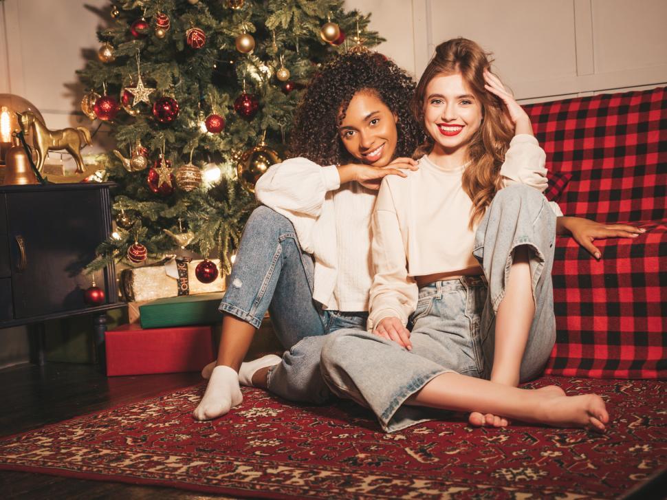 Free Image of Two women sitting on a couch next to a christmas tree 