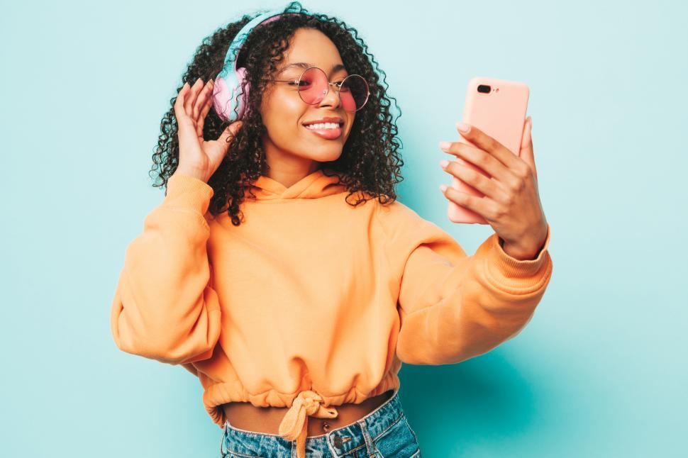 Free Image of A woman wearing headphones and holding a phone 