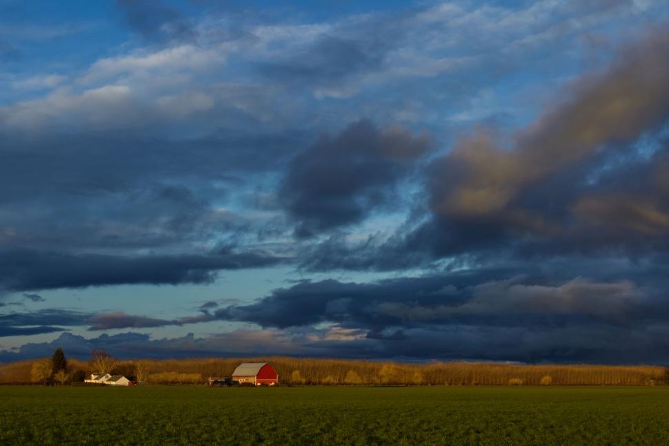 Free Image of Rural farmland with red barn under cloudy sky 