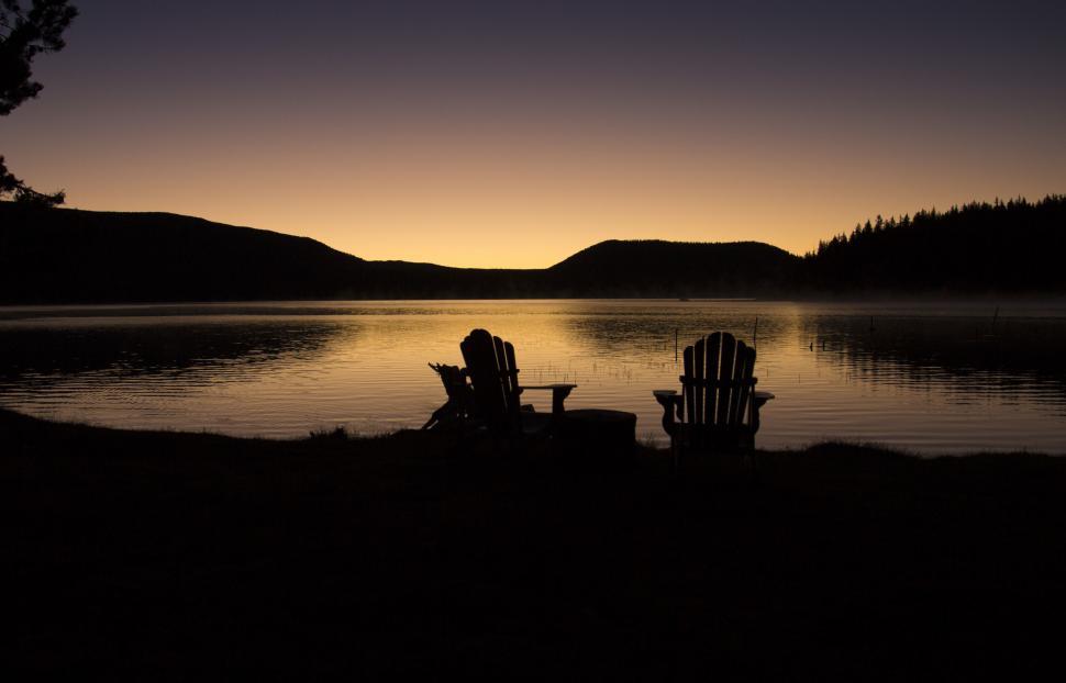 Free Image of Silhouette of chairs by a lake at sunset 