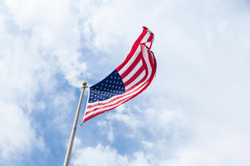 Free Image of American flag waving under blue sky with clouds 