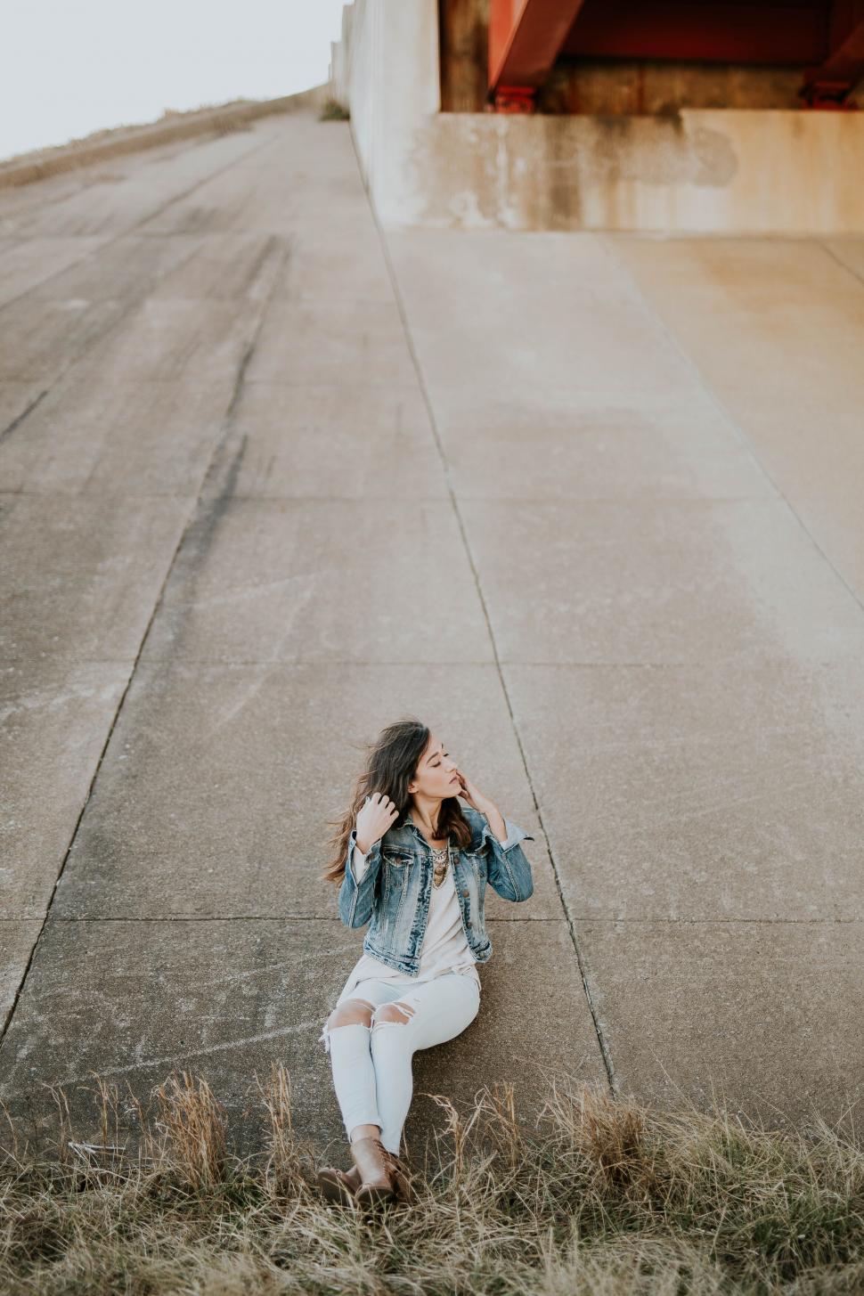 Free Image of Young woman sitting on a sloped concrete wall 