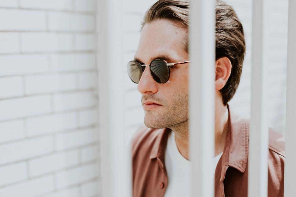 Free Image of Man in sunglasses by a white brick wall 