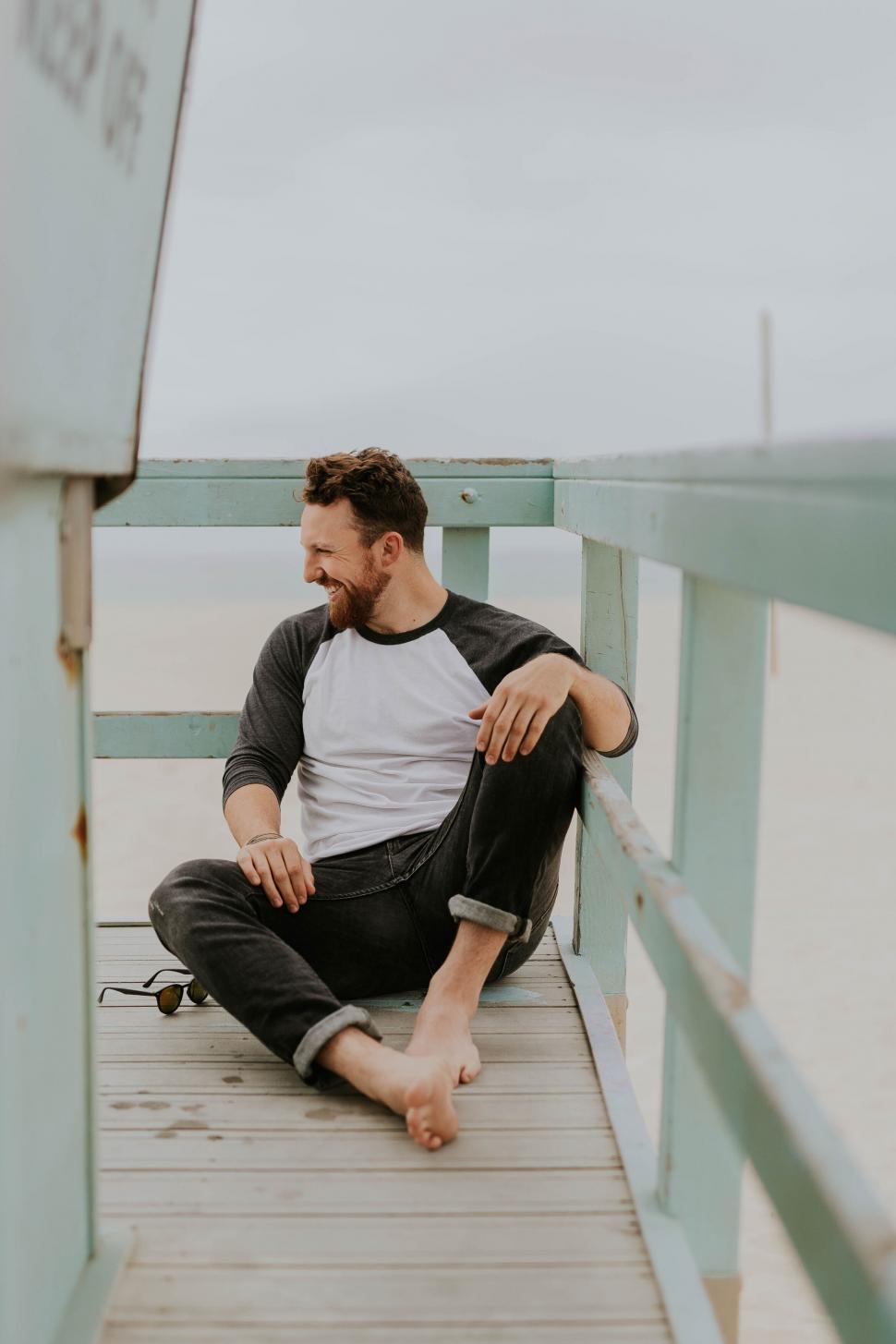 Free Image of Casual man sitting on beach pier railing 