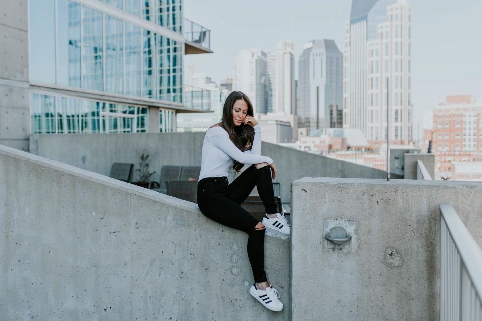 Free Image of Woman sitting on concrete ledge in city 