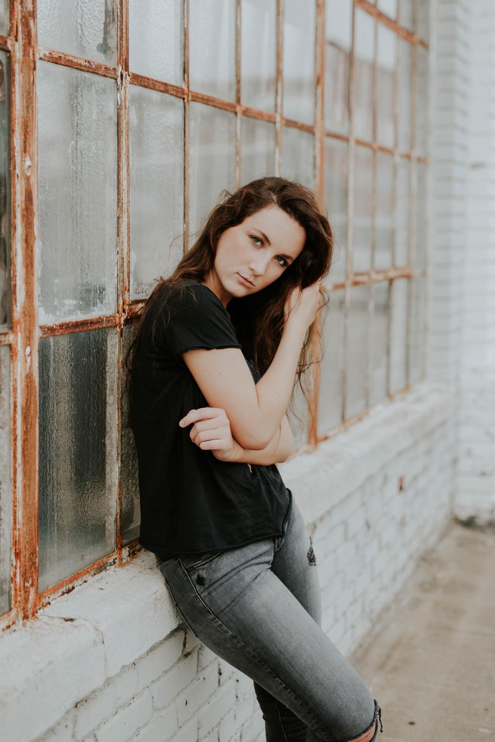 Free Image of Young woman posing by a weathered window 