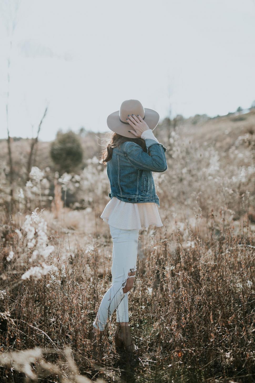 Free Image of Woman in field holding hat looking away 