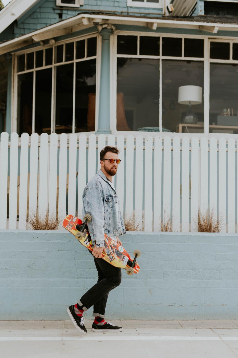 Free Image of Skater with denim jacket walking in front of house 