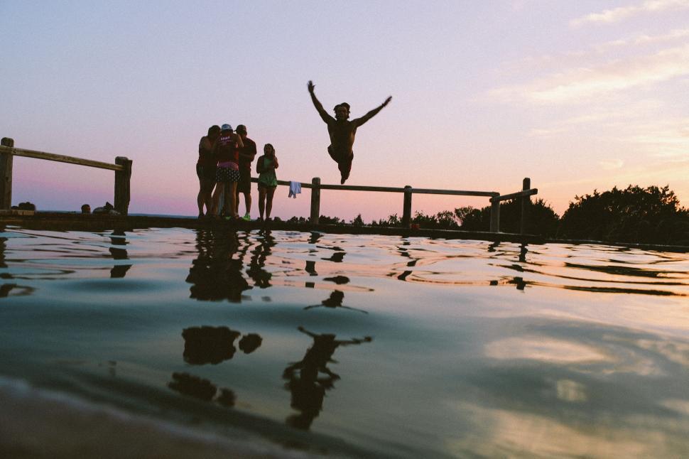 Free Image of Silhouetted jump into water at sunset 