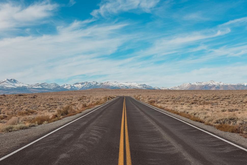 Free Image of Desert road stretching into snow-capped mountains 