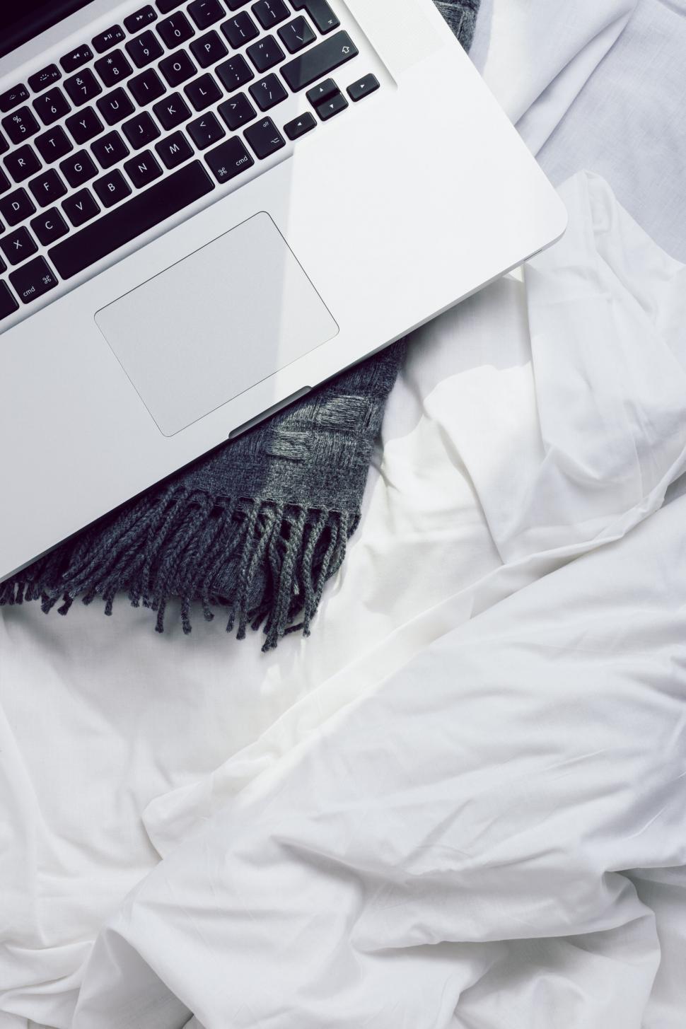 Free Image of Laptop on bed with gray throw and white sheets 