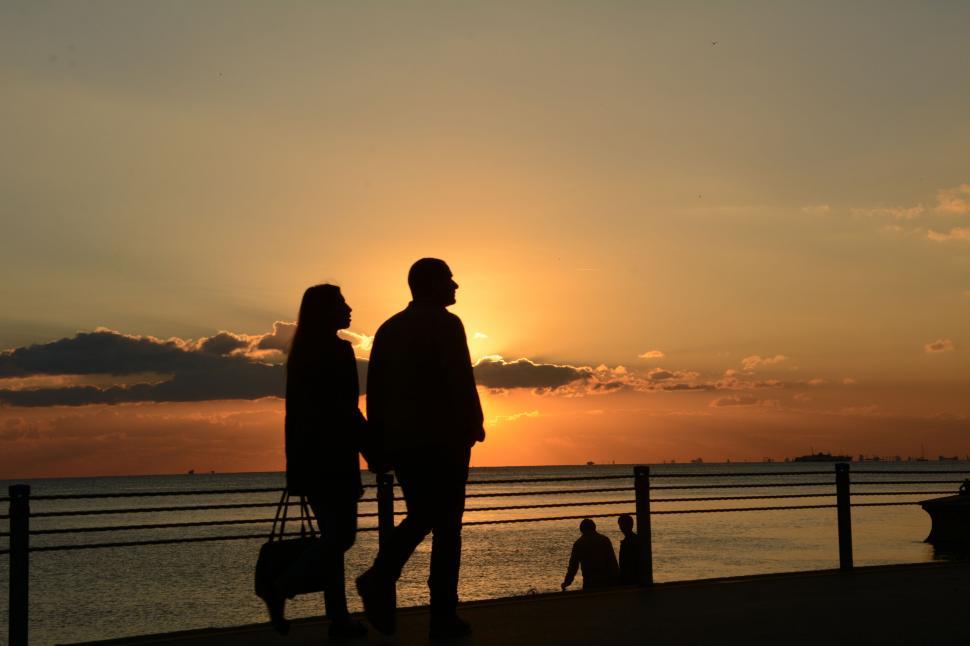 Free Image of Silhouetted couple walking by seaside at sunset 