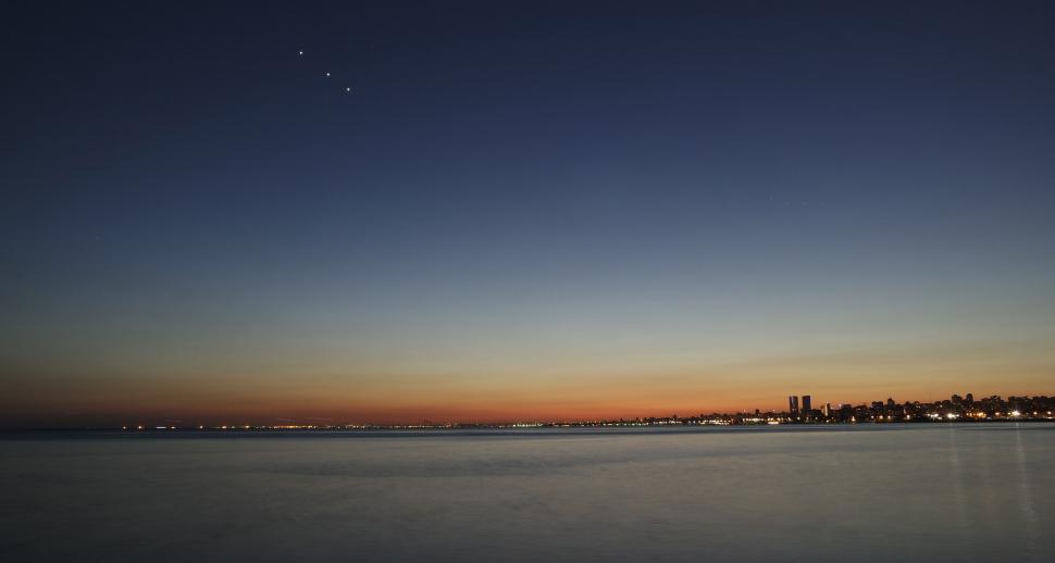 Free Image of Sunset over calm sea with city skyline 
