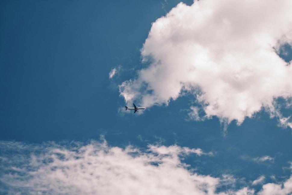 Free Image of Airplane flying through cloudy blue sky 