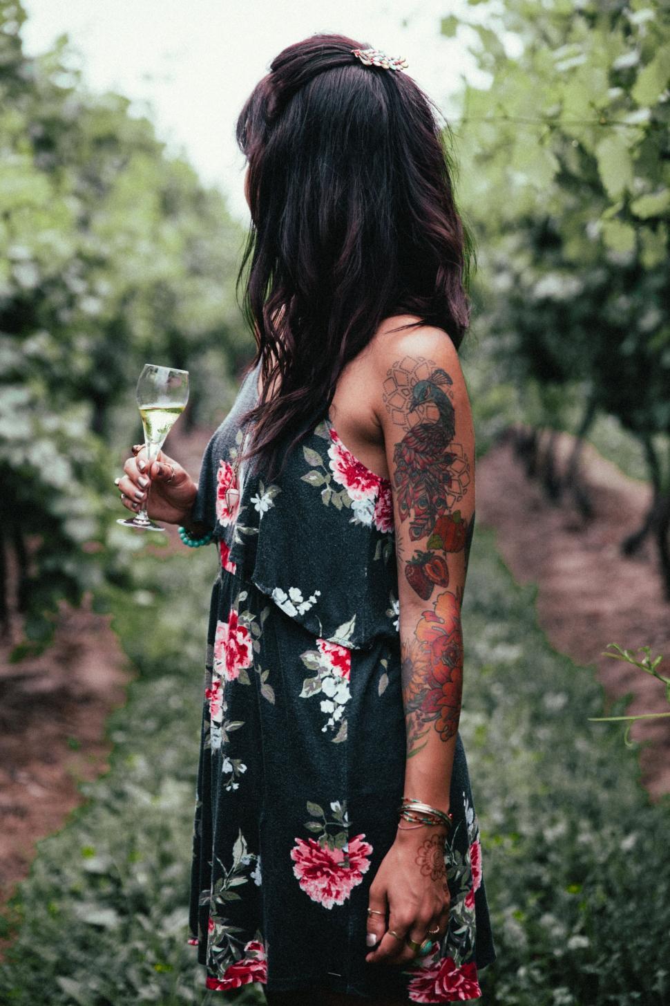 Free Image of Woman with tattoos holding wine in vineyard 