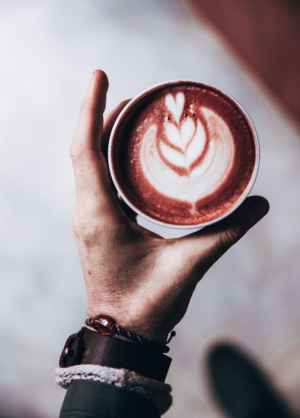 Free Image of Hand holding a cup of coffee with art 