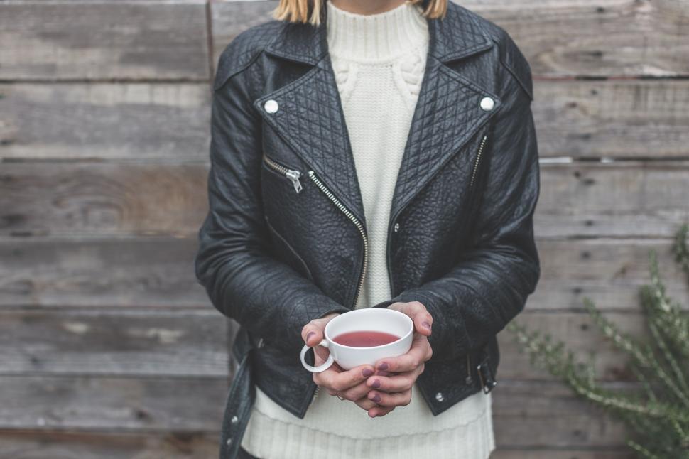 Free Image of Woman holding a cup of tea in a leather jacket 