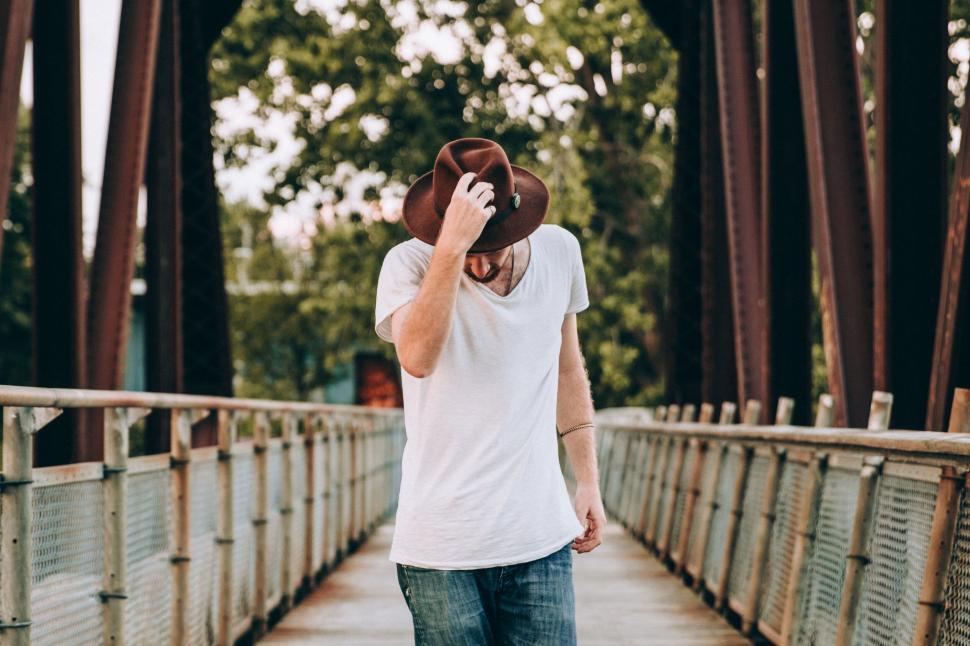 Free Image of Man holding hat on bridge with blurred face 